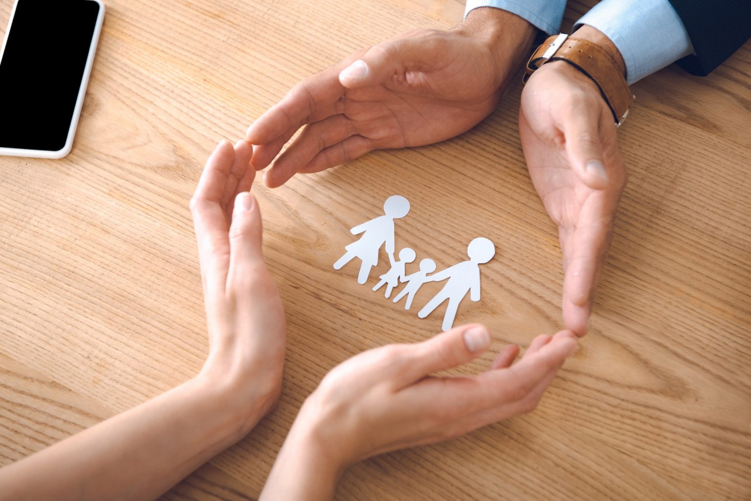 partial view of insurance agents and female hands with family paper model on wooden tabletop, family